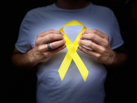 Ein Mann, dessen Gesicht nicht zu sehen ist, hält eine gelbe Schleife in der Hand.