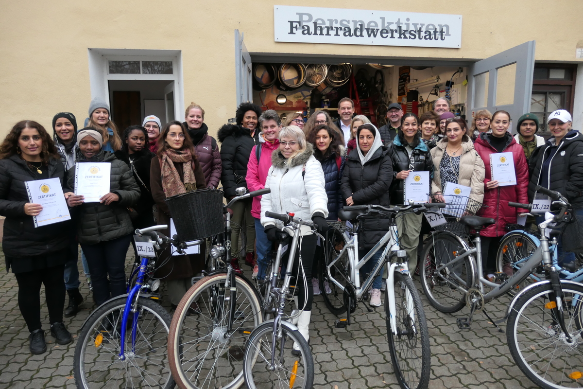 Viele Personen stehen vor dem Einganstor der Fahrradwerkstatt, vor ihnen stehen Fahrräder.