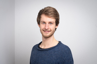 Ein Porträt eines jungen Mannes, der in die Kamera lächelt.