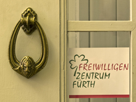 Nahaufnahme eines Türklopfers an einer Eingangstür, daneben hängt das Logo des Freiwilligenzentrums Fürth.