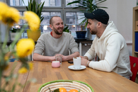 Zwei junge Männer sitzen an einem Tisch und sprechen miteinander.