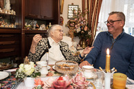 Eine ältere Dame unterhält sich in einem Wohnzimmer mit einem Mann. Er lächelt sie an.