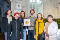Sechs Teammitglieder, darunter fünf Frauen und ein Mann, stehen vor dem Eingang des Freiwilligenzentrums und präsentieren die Plakette, die das Qualitätssiegel ausweist und neben den Eingang gehängt wird.