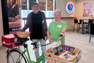 Eine ältere Frau und ein Mann mittleren Alters stehen im Foyer des Kinos. Die Frau hält ein Fahrrad fest, das im Freiwilligenzentrum für Öffentlichkeitsaktionen als Flyerstand genutzt wird.