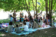 Eine Gruppe Familien sitzen unter einem Baum im Schatten im Park.