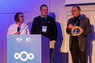 Jury-Mitglied Maddalena Falzoni, Josef Dorn-Schwarzkopf und Günter Krauß auf der Bühne des Nextcloud Summit. Günter Krauß hält den Award in der Hand und spricht in ein Mikro und spricht zum Publikum.
