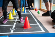Zu sehen ist ein Hüpfspiel, das gerade aktiv bespielt wird, wobei die beteiligten Kinder und Erwachsenen nur knieabwärts zu sehen sind.