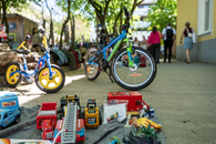 Zu sehen sind verschiedene Spielzeugautos auf einer Decke und zwei Kinderfahrräder im Hinterhof von MIO. Im Hintergrund laufen drei Besucher zum Hoftor.