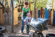 Eine Erzieherin und ein Junge schieben zusammen eine Schubkarre.