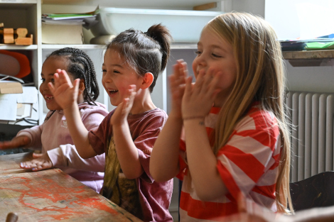 Kinder sitzen an einem Tisch, lachen und klatschen in die Hände.