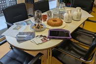 Zu sehen ist ein gedeckter Tisch mit Gebäck, Warmgetränken in Kannen und Geschirr. Dazu liegt Informationsmaterial zum Thema Medienpädagogik mit kleinen Kindern und ein Tablet bereit.