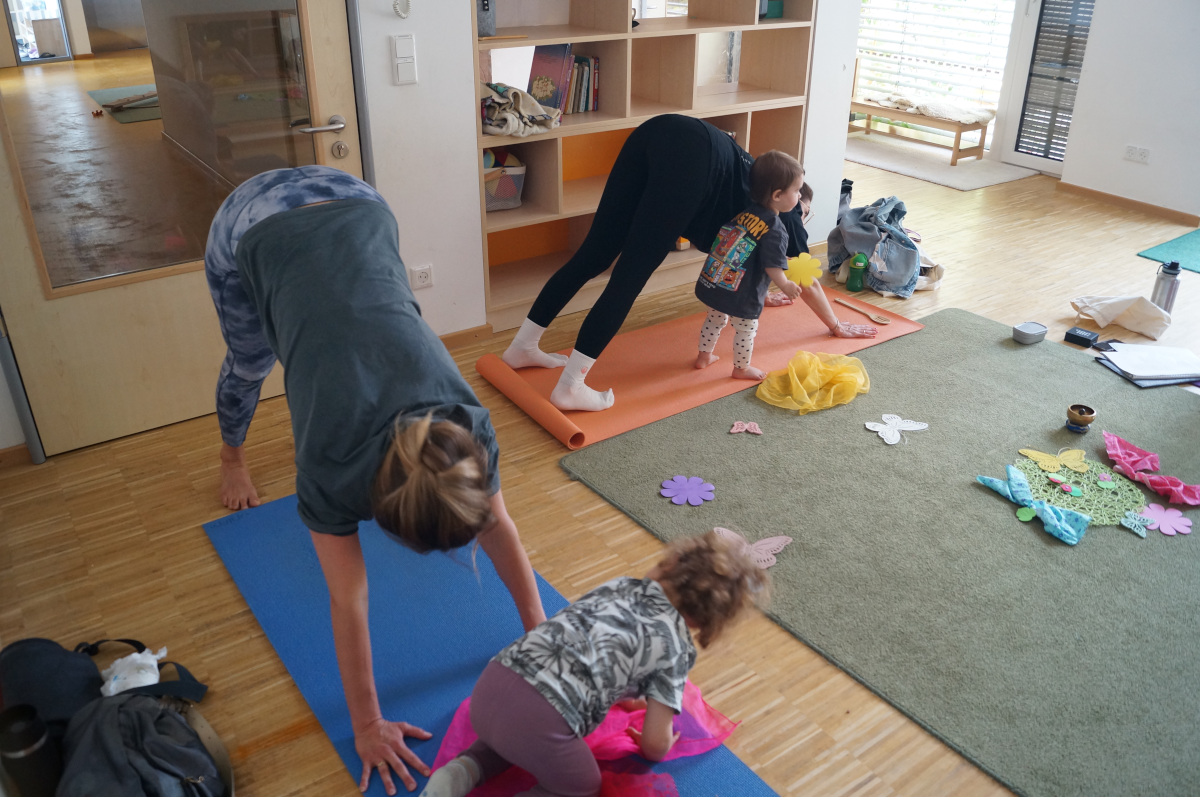 Auf Yogamatten machen Frauen Übungen, ihre Kinder sitzen mit auf der Matte.