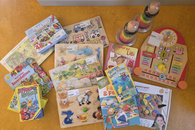 Das Bild zeigt einige der Spiele, die an die Kita MIRA gespendet wurden, unter anderem zwei Bücher, zwei Stapeltürme, fünf Gesellschaftsspiele und vier Holzpuzzle