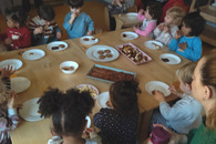 Mehrere Krippenkinder, augenscheinlich unterschiedlicher Herkunft, sitzen gemeinsam mit einer Erzieherin an einem Tisch und feiern das Zuckerfest.