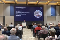 Vortragssitiation mit Blick auf eine große Leinwand, Publikum mit Rücken zur Kamera.