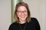 Porträt einer jungen Frau mit schulterlangen, dunkelblonden Haaren und Brille.