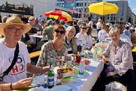 Menschen sitzen an gedeckten Tischen unter freiem Himmel und freuen sich.