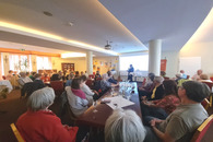 Ein gefüllter Saal mit vielen Menschen an Tischen.