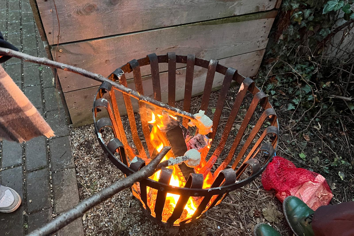 Zwei Kinder halten Stockbrot über einen Feuerkorb.